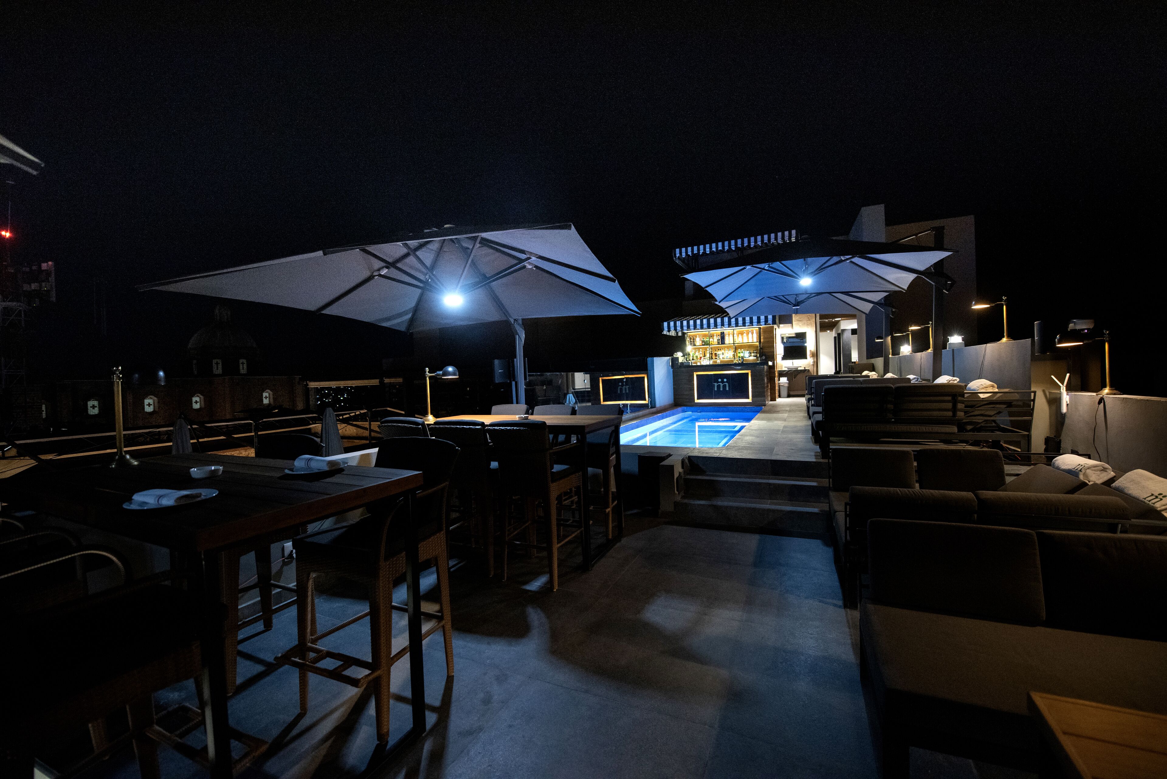 An outdoor bar area with tables, chairs, umbrellas, and a pool.