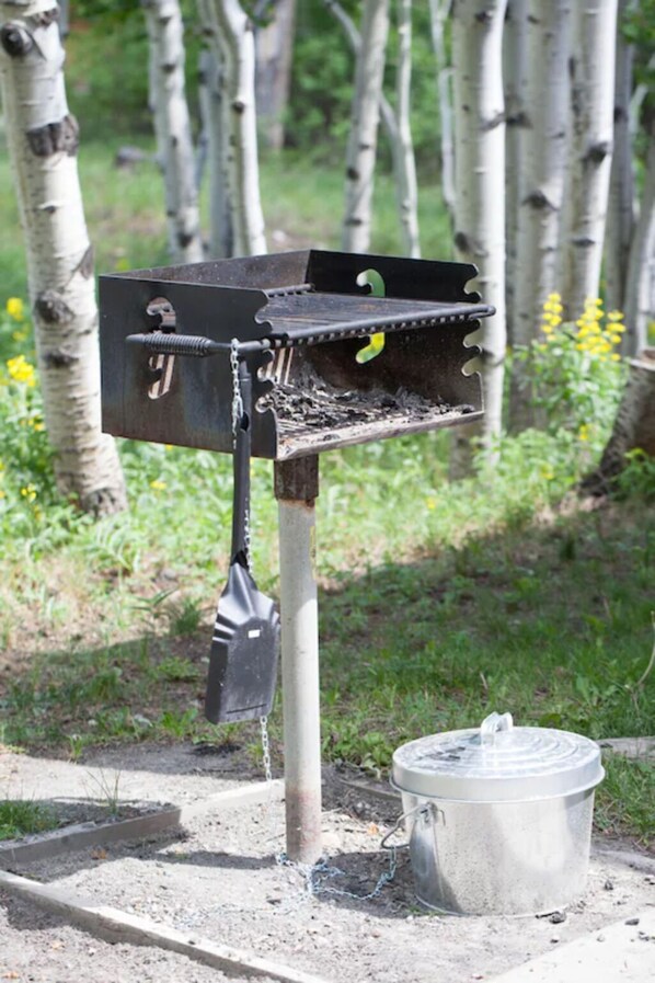 A metal bird feeder attached to a pole with a chain, a metal bucket, and a shovel on the ground.