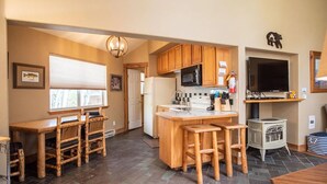 A kitchen with wooden cabinets, a central island with stools, a stove, and a television. - Mt. Shavano Chalet at Creekside chalets (Salida)