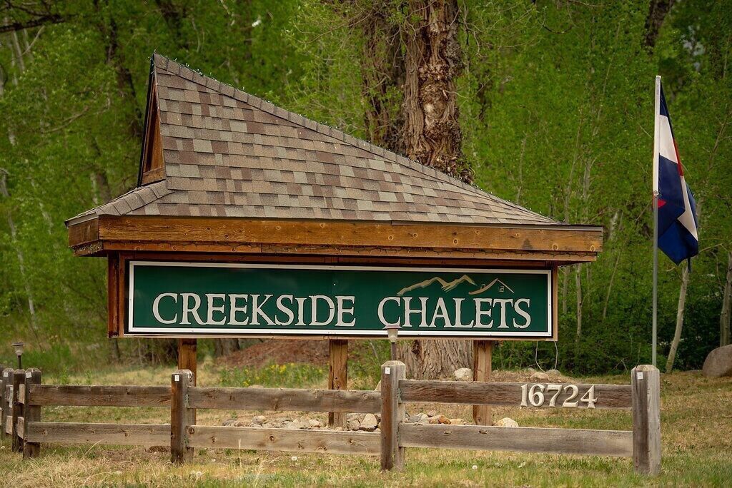 Un chalet en bois avec une enseigne verte portant l’inscription « Creekside Chalets » et un drapeau.