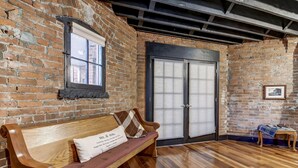 A room with a wooden bench, a window, a door, and a small table with a blanket. - Holly & Matt Suite @ Three Pines Petersburg (Petersburg)