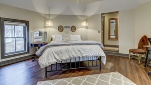 A bedroom with a large bed, a desk, and a chair. There is a window, a mirror, and a door. - Holly & Matt Suite @ Three Pines Petersburg (Petersburg)