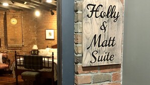 A sign reading "Holly & Matt Suite" in a room with a brick wall and a bed with a wooden headboard. - Holly & Matt Suite @ Three Pines Petersburg (Petersburg)