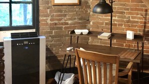 A rustic room with exposed wooden beams, a brick wall, a dining table with chairs, a framed picture, and a window with blinds. - Holly & Matt Suite @ Three Pines Petersburg (Petersburg)