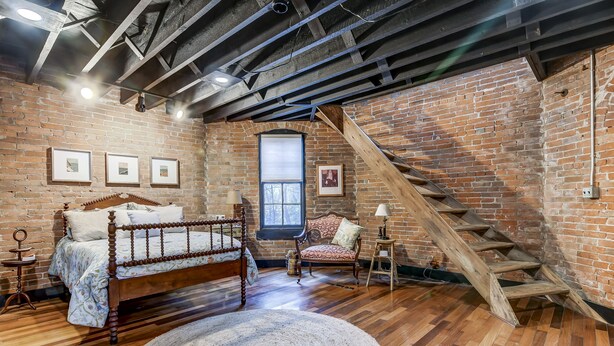 A bedroom with a wooden bed, a large window, a brick wall, and a wooden staircase. - Holly & Matt Suite @ Three Pines Petersburg (Petersburg)