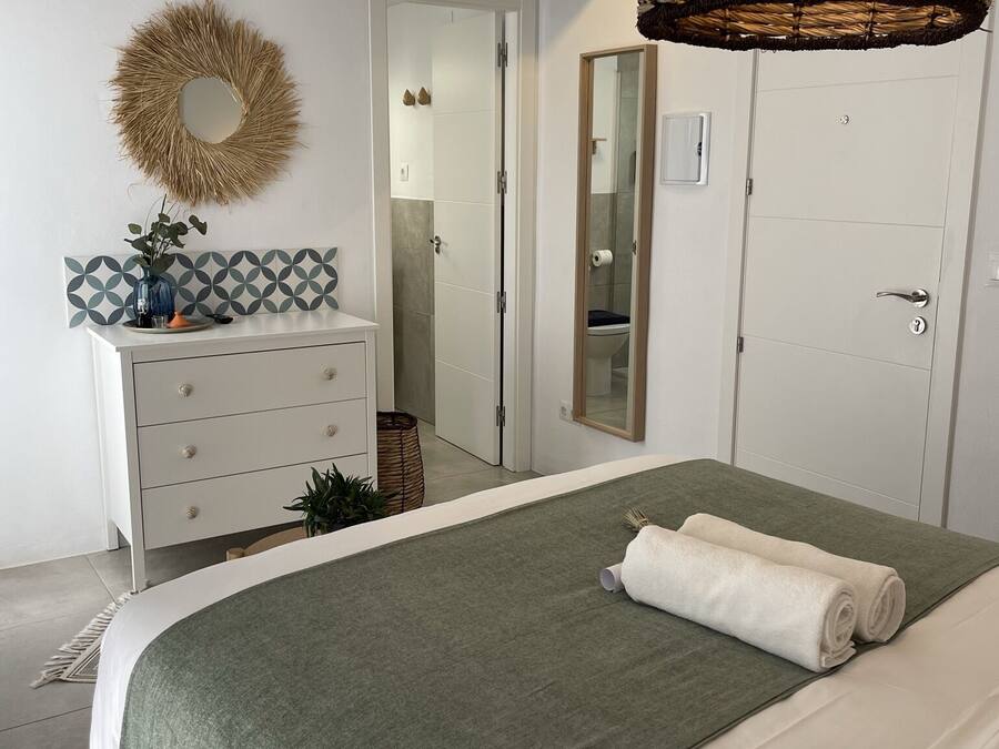 Un dormitorio con cama, cómoda, espejo y puerta que da a un baño.