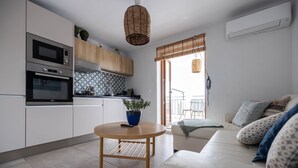 Eine moderne Küche mit Einbaugeräten, einem Esstisch mit Pflanze und einem Wohnbereich mit Sofa und Kissen.