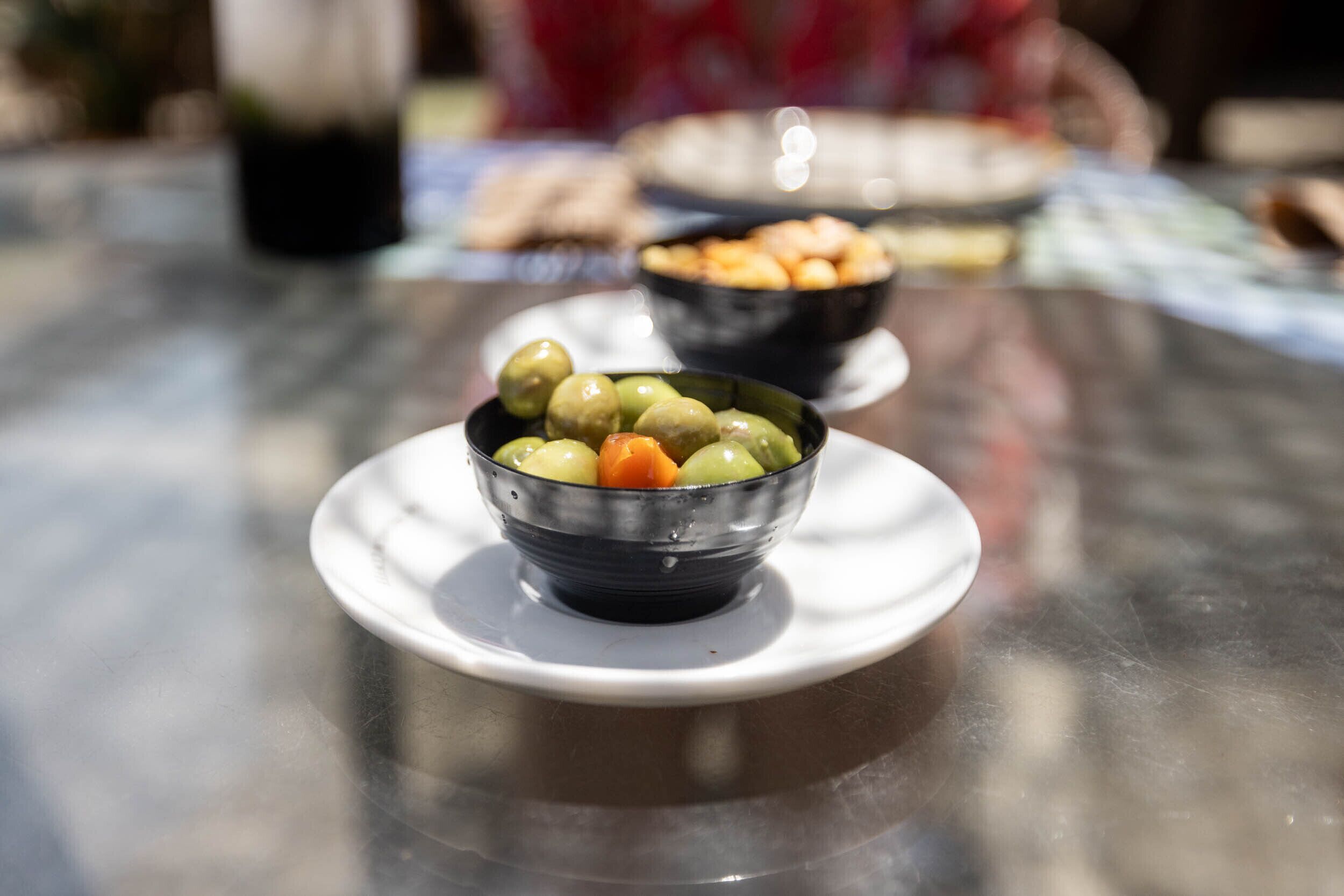 Une table avec un bol d’olives sur une assiette blanche.