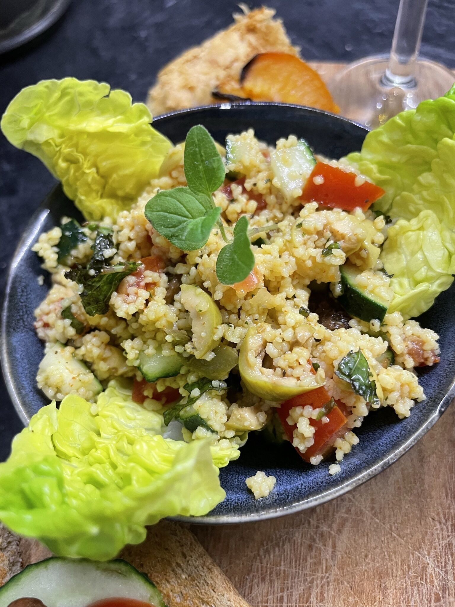 A bowl of couscous salad with vegetables and mint leaves.