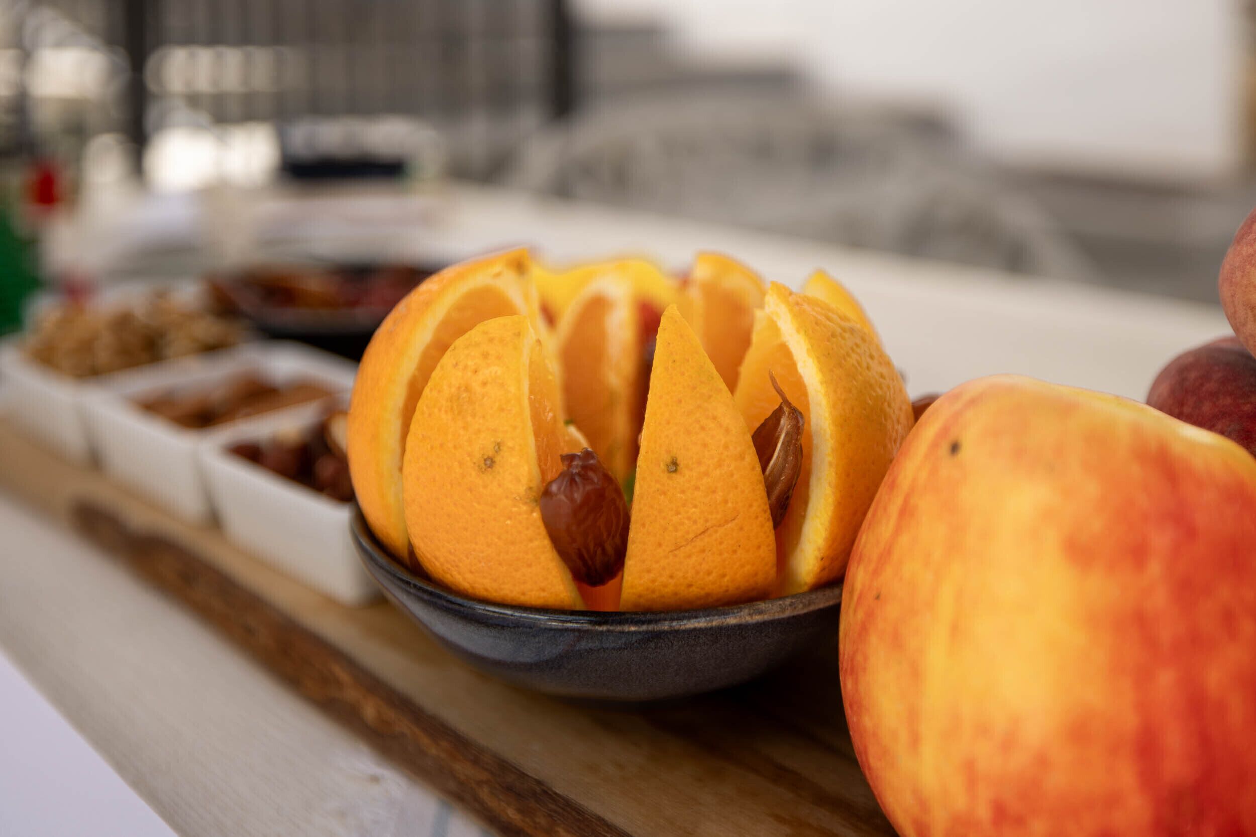 Un cuenco con rodajas de naranja y un melocotón entero sobre una superficie de madera.