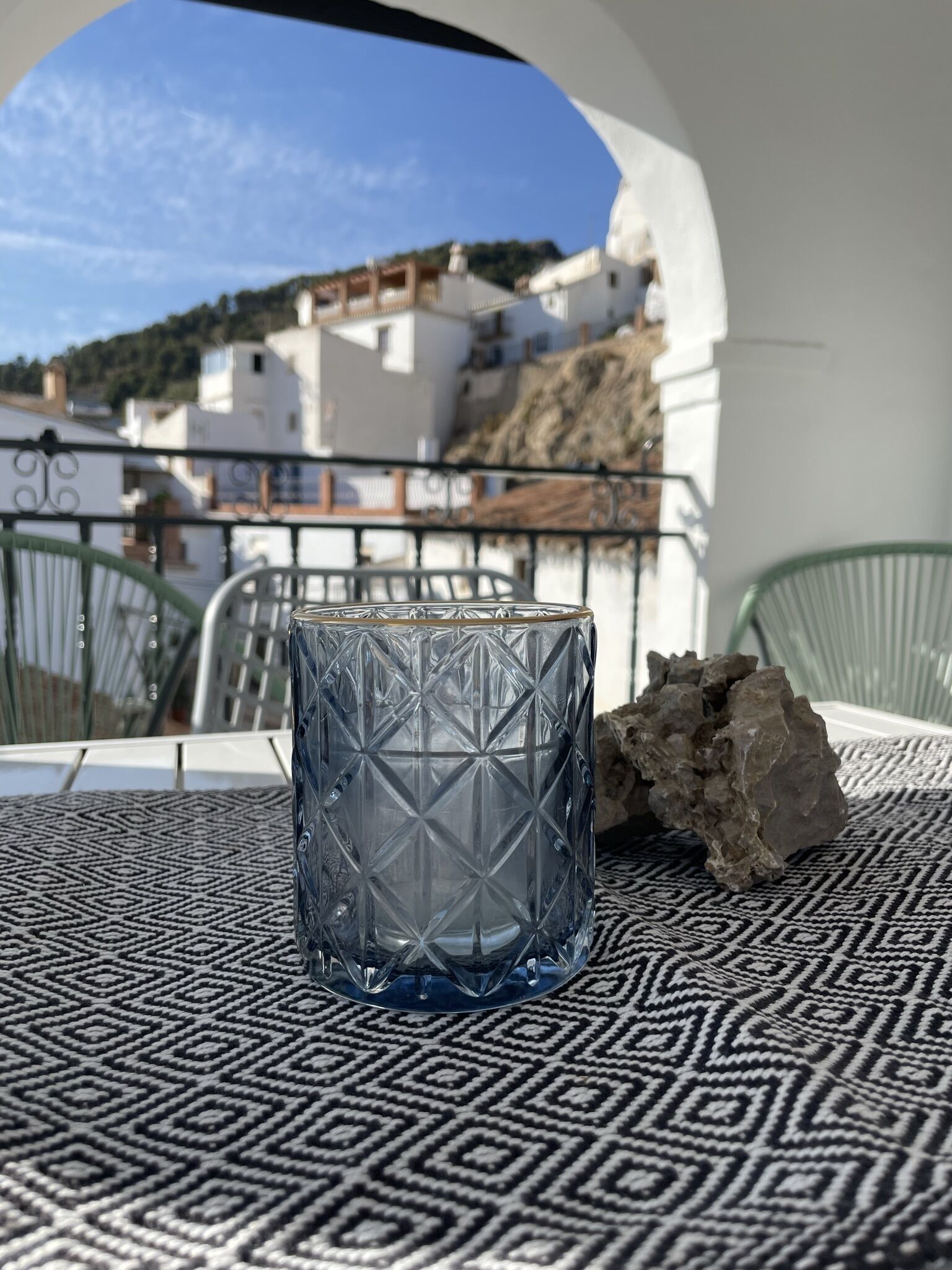 A glass table with a geometric pattern, a rock, and a view of white buildings and a hill in the background.