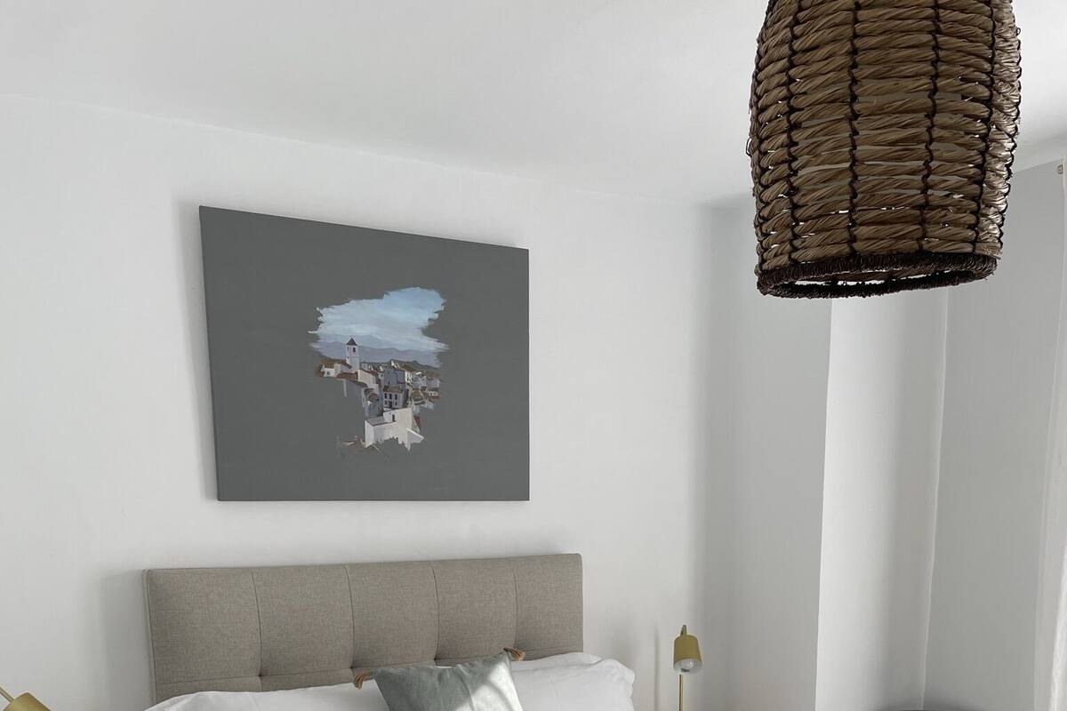 Un dormitorio moderno con cama, mesitas de noche, una silla y una lámpara colgante.
