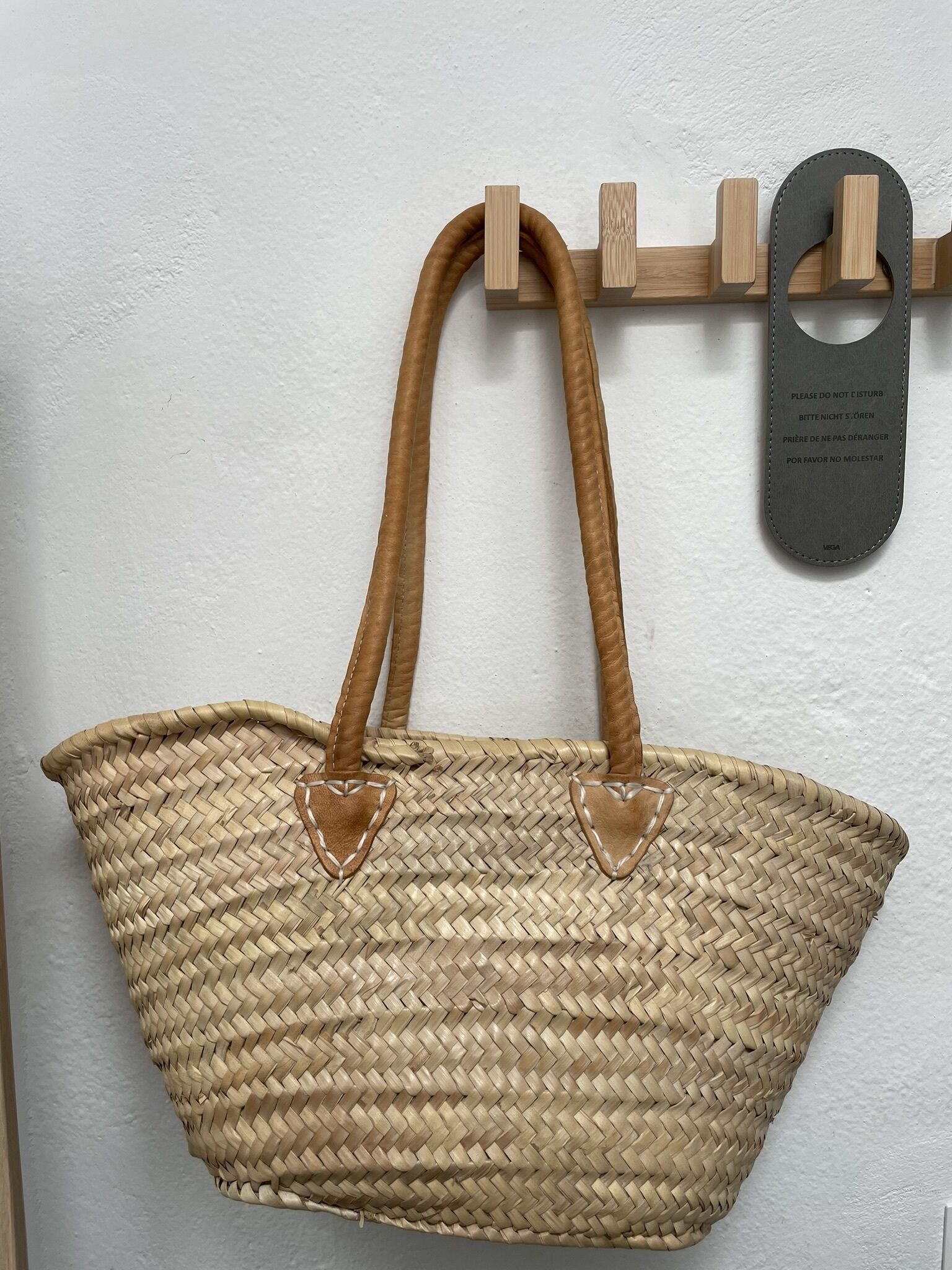 A woven tote bag hanging on a wooden rack with a metal plaque.