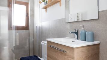 Un baño moderno con tocador de madera, un lavabo blanco y un espejo grande.