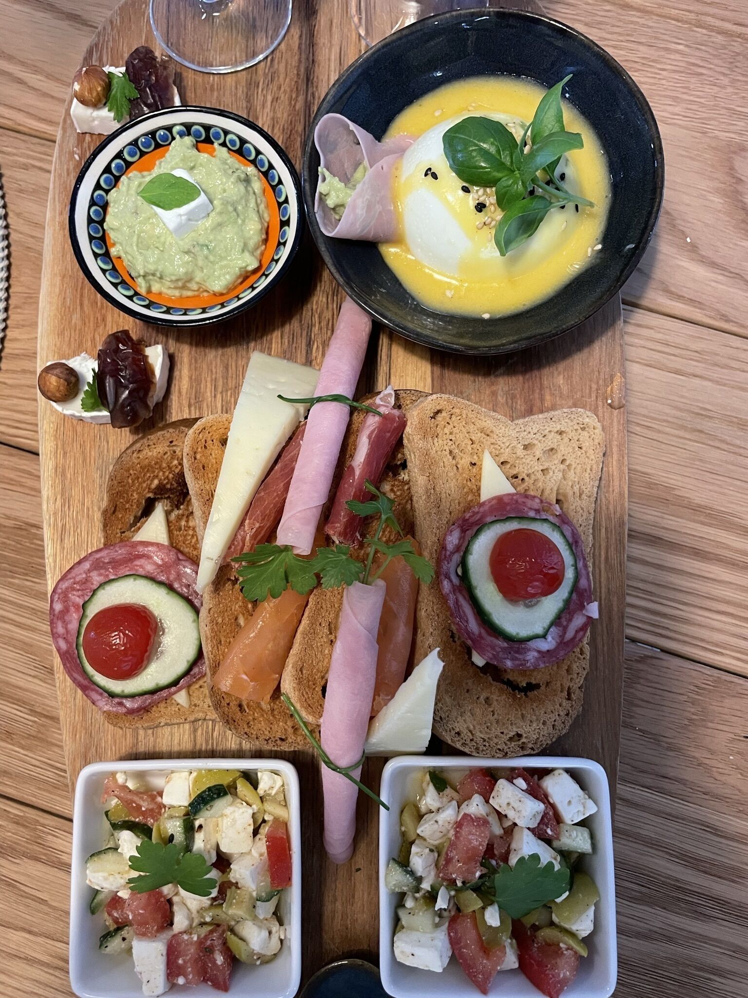 A wooden board with various food items including bread, cured meats, and a bowl of salad.