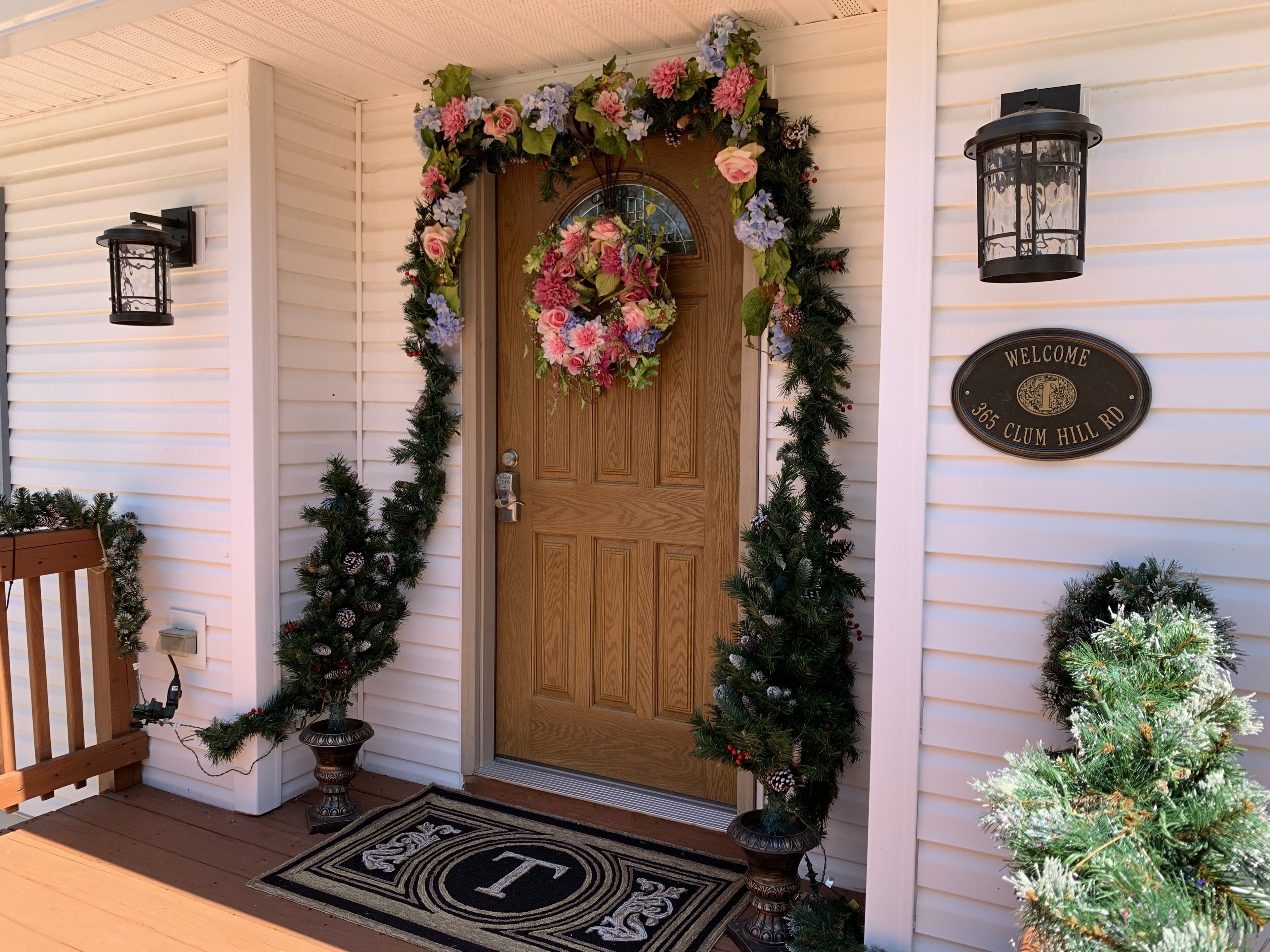 Una puerta de madera con un adorno floral, un cartel de bienvenida y un árbol de Navidad.