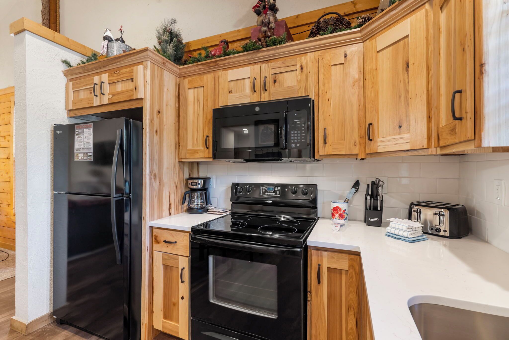 A kitchen with wooden cabinets, a black refrigerator, a microwave, a stove, and a toaster.