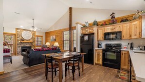 A spacious kitchen with wooden cabinets, a dining area with a table and chairs, and a living room with a sofa and fireplace. - 2 BD Cabin near Branson Theatre District - Gas Fireplace & Whirlpool Tub,Ticket Discounts! (Branson)
