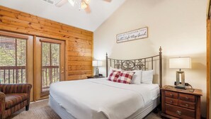 A bedroom with a large bed, wooden walls, a ceiling fan, a window with blinds, a nightstand with a lamp, and a sign on the wall. - 2 BD Cabin near Branson Theatre District - Gas Fireplace & Whirlpool Tub,Ticket Discounts! (Branson)