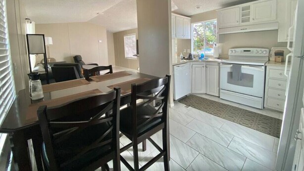 A compact kitchen with white cabinets, a stove, and a dining area with a table and chairs.