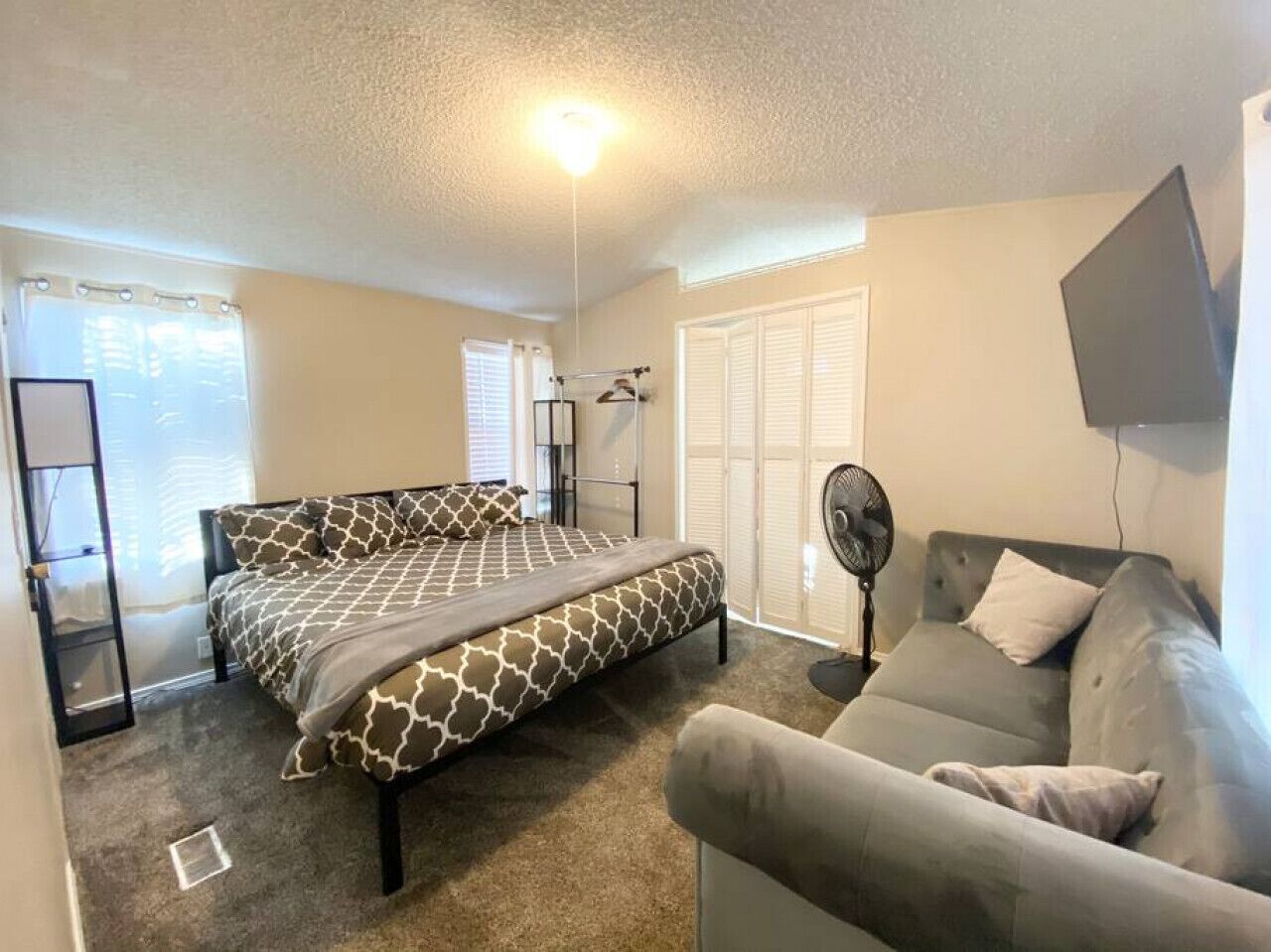 A bedroom with a bed, a sofa, a standing fan, and a ceiling light.