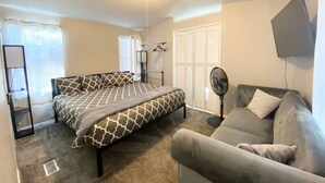A bedroom with a bed, a sofa, a standing fan, and a ceiling light.