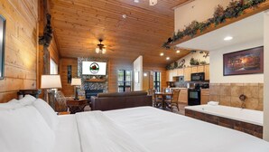 A hotel room with a large bed, a fireplace, a dining area, and a kitchen. - Romantic Walk-in Cabin for Two in the Heart of Branson - Jacuzzi Tub (Branson)