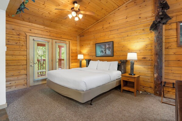 A wooden-paneled bedroom with a bed, two bedside lamps, a ceiling fan, and a framed picture on the wall.