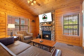 A cozy log cabin interior with a stone fireplace, wooden walls, and a comfortable seating area.
