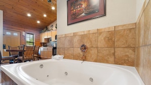 A spacious bathroom with a large bathtub, wooden ceiling, and tiled walls. - Romantic Walk-in Cabin for Two in the Heart of Branson - Jacuzzi Tub (Branson)