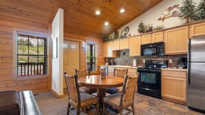 A wooden-paneled kitchen with a round dining table and chairs, a refrigerator, stove, and microwave. - Romantic Walk-in Cabin for Two in the Heart of Branson - Jacuzzi Tub (Branson)