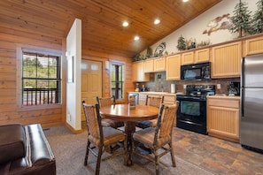 A wooden-paneled kitchen with a round dining table and chairs, a refrigerator, stove, and microwave.