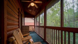 Eine Holzveranda mit Deckenventilator, Holzstühlen und Blick auf den Wald.