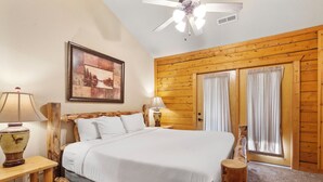 Ein Schlafzimmer mit einem hölzernen Kopfende, einem Bett mit weißer Bettwäsche, zwei Nachttischlampen, einem Deckenventilator und einem gerahmten Bild an der Wand.