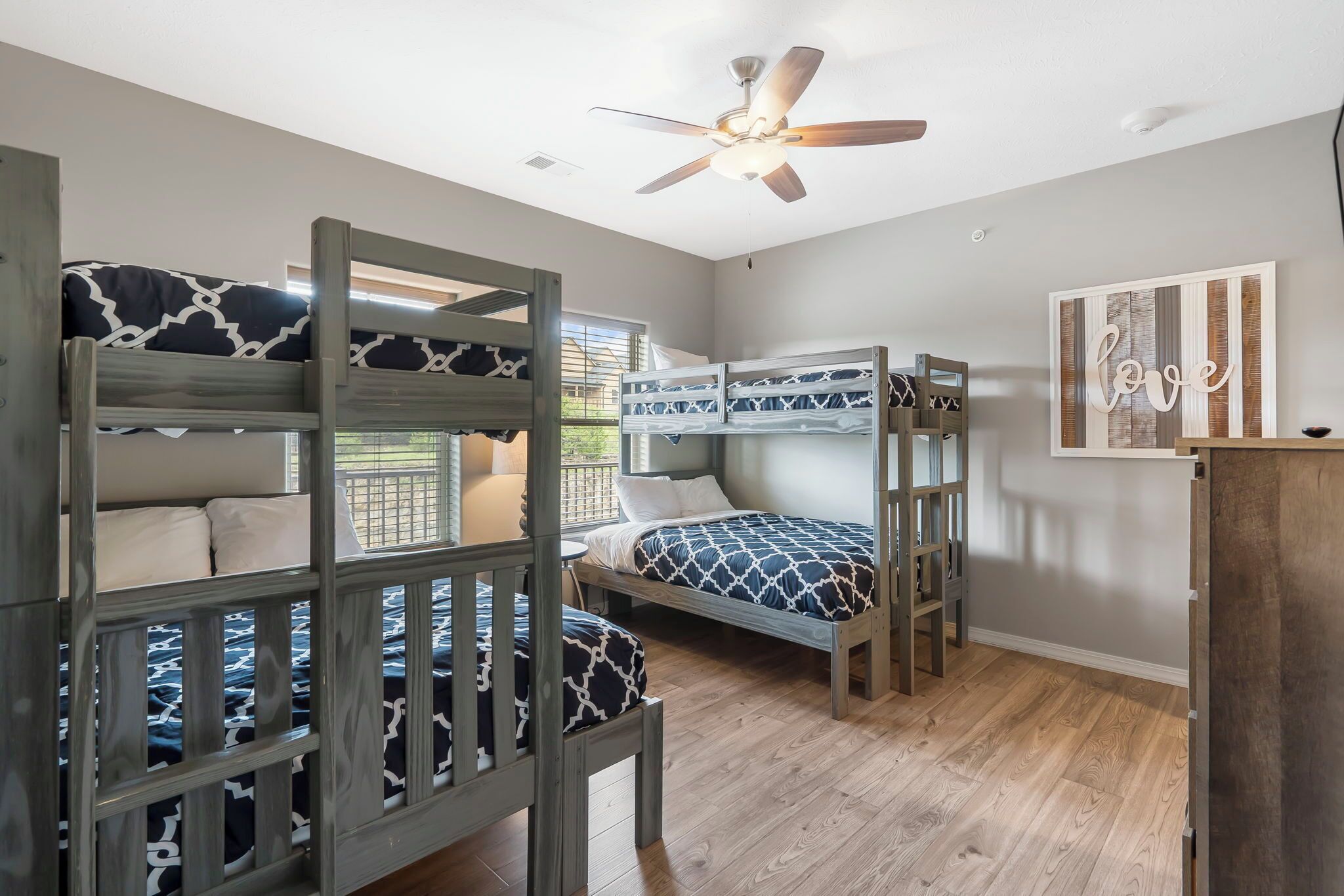 A room with bunk beds, a ceiling fan, and a 'love' wall art piece.