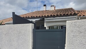A gated entrance with a concrete wall, a metal gate, and a tiled roof in the background. - Air-conditioned, fully renovated duplex with private terrace (Lunel)