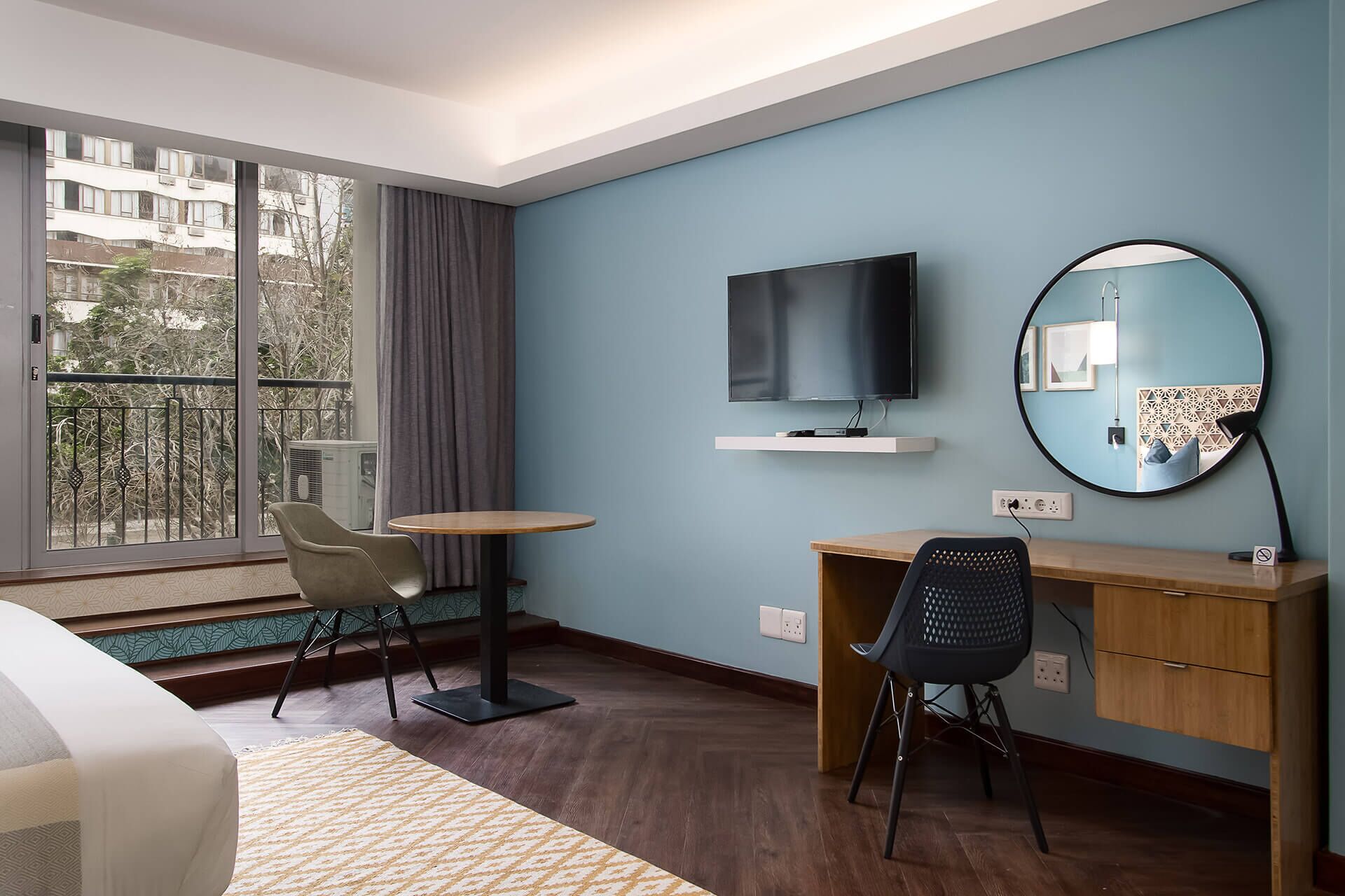 Ein Hotelzimmer mit großem Fenster, Schreibtisch, Stuhl, Fernseher und Spiegel.