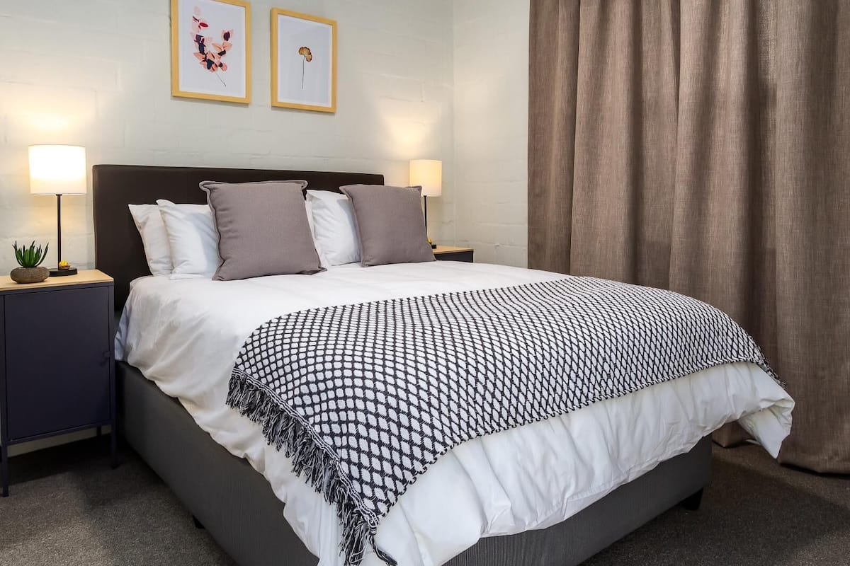 A neatly made bed with a patterned blanket, two bedside tables with lamps, and two framed pictures on the wall.
