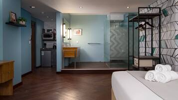 A hotel room with a bed, a bathroom with a shower, a kitchenette, and a wardrobe with towels.