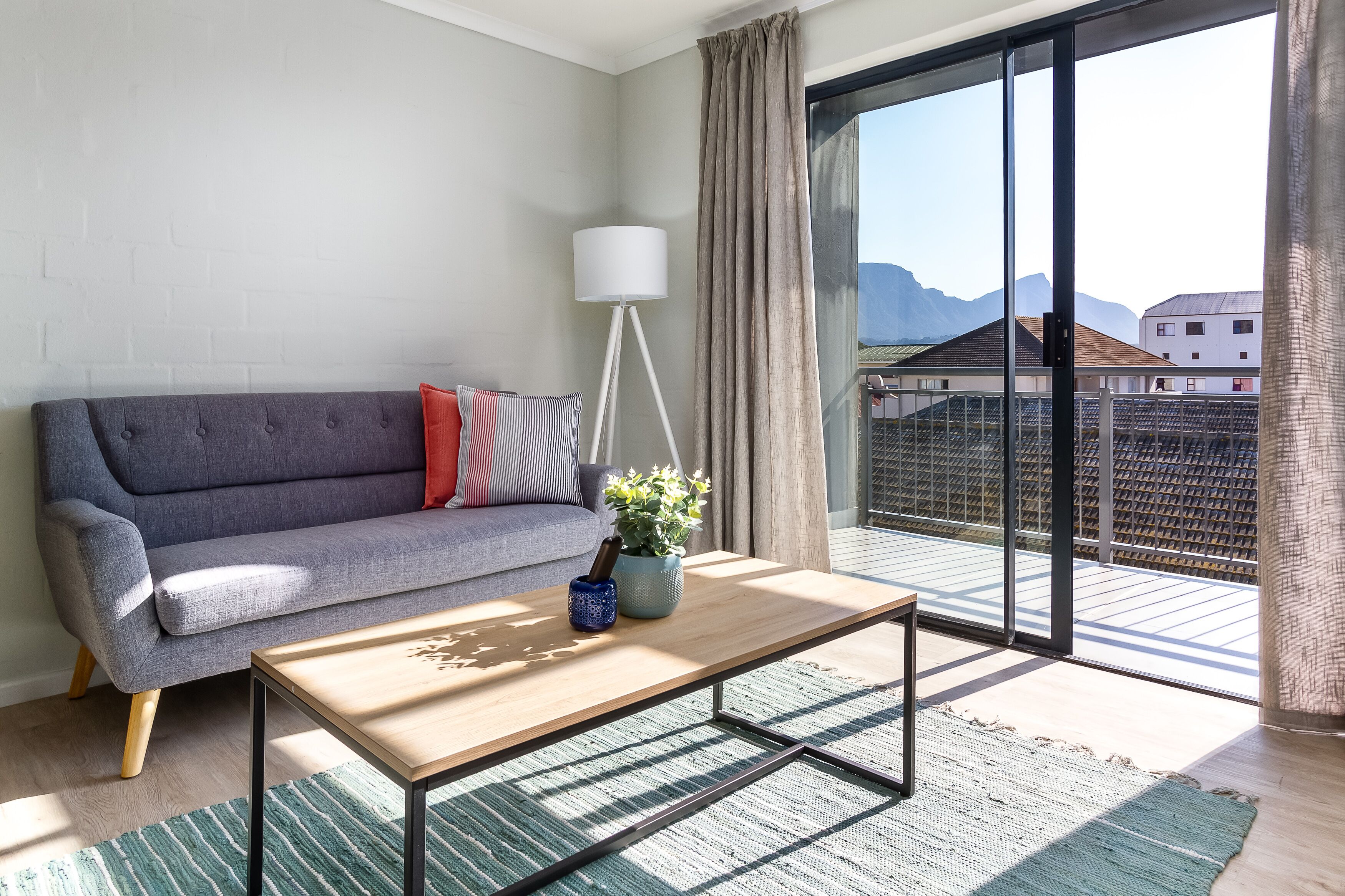 Een moderne woonkamer met een grijze bank, een houten salontafel en een potplant.