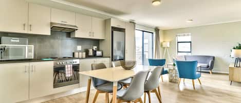 A modern kitchen with a dining area, featuring a central island, wooden cabinets, and a large window.