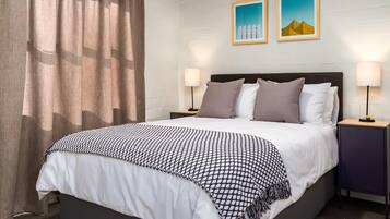 Una cama bien hecha con una colcha estampada, dos lámparas de noche y vistas de la ciudad a través de la ventana.