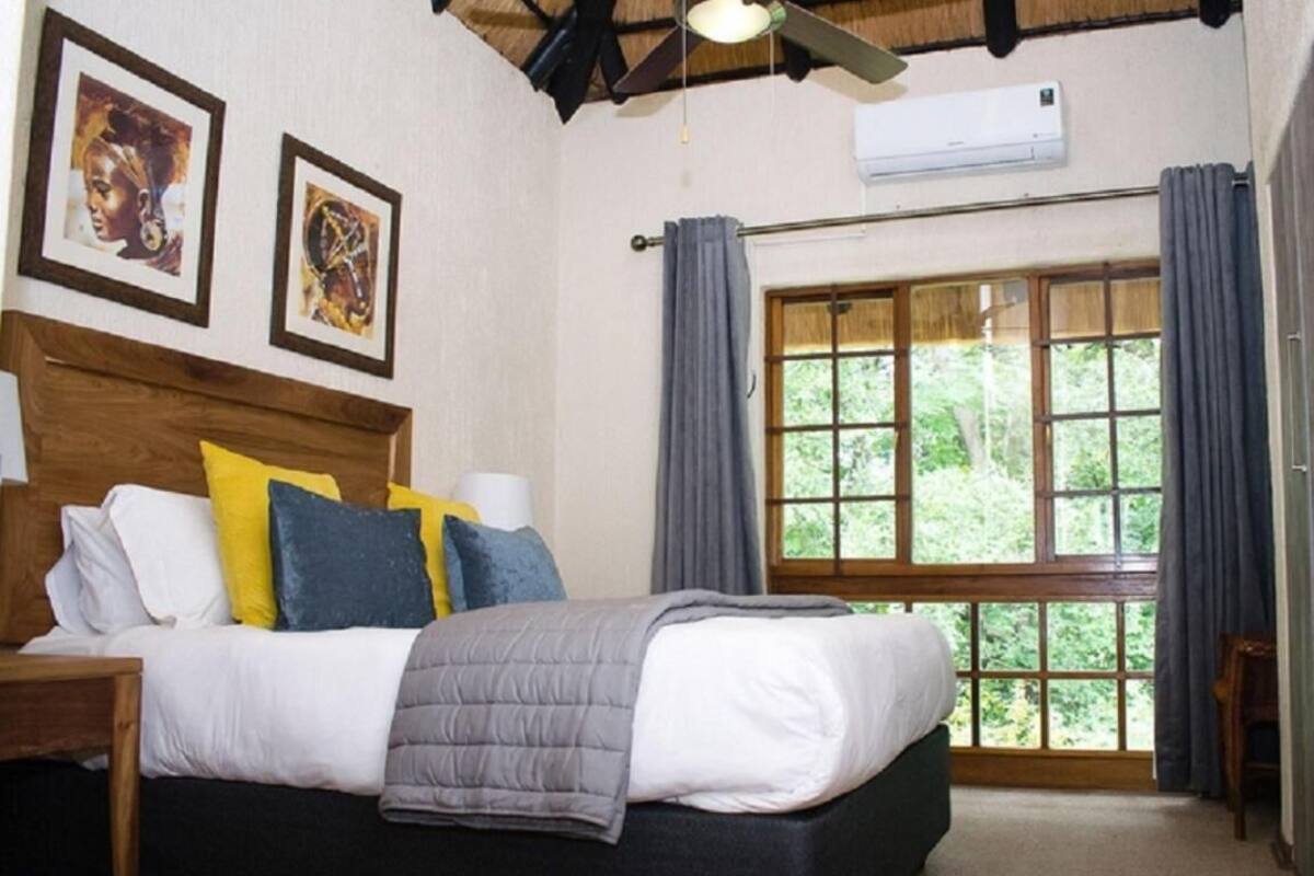 A bedroom with a bed, a nightstand, a ceiling fan, a window with curtains, and framed artwork on the wall.