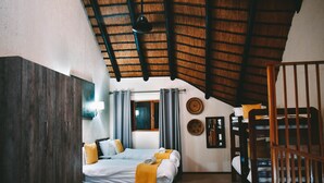 Een slaapkamer met een stapelbed, een kledingkast, een bed met een gele plaid, een houten plafond en een raam met gordijnen.