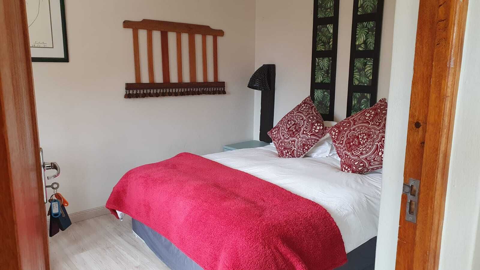 A bedroom with a bed, a red blanket, patterned pillows, a wooden headboard, and a door with keys hanging on it.