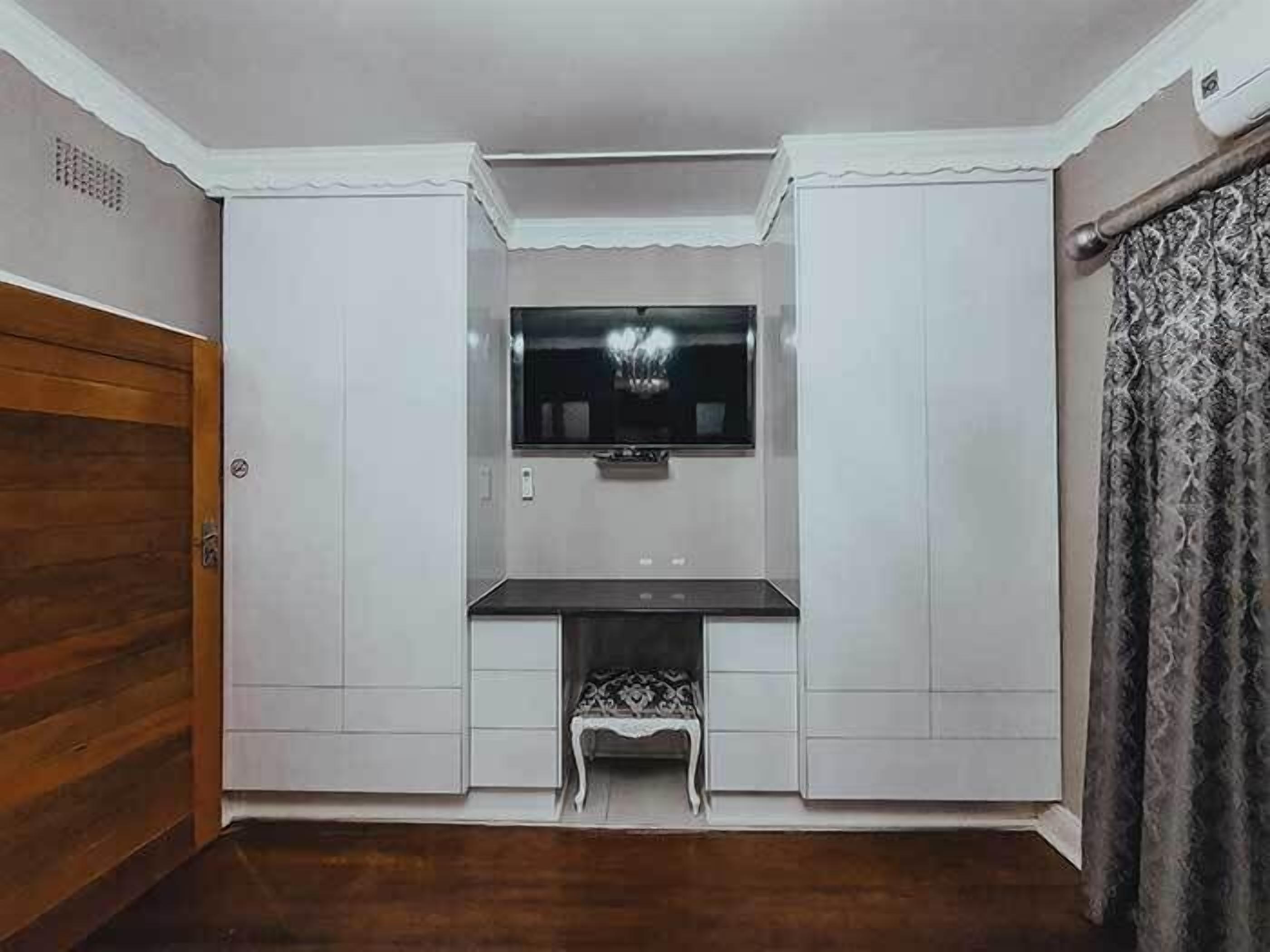 A compact room with a built-in TV, a small bench, and a wooden door.