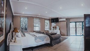 Een ruime slaapkamer met een groot bed, een nachtkastje, een dressoir en een televisie.
