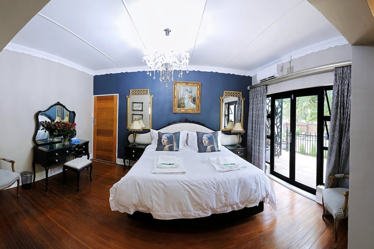A bedroom with a large bed, a chandelier, a dresser, and a view of the outdoors.