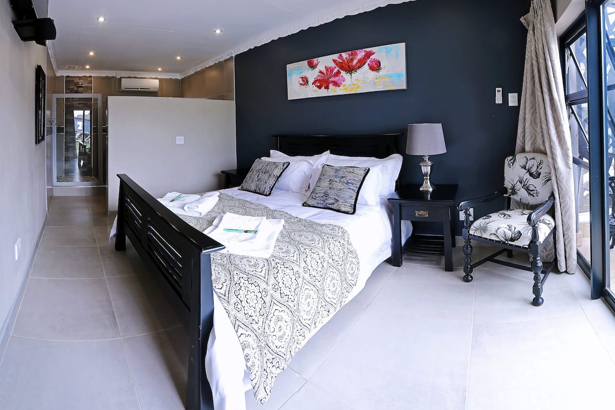 A modern bedroom with a large bed, a nightstand, a chair, and a painting on the wall.