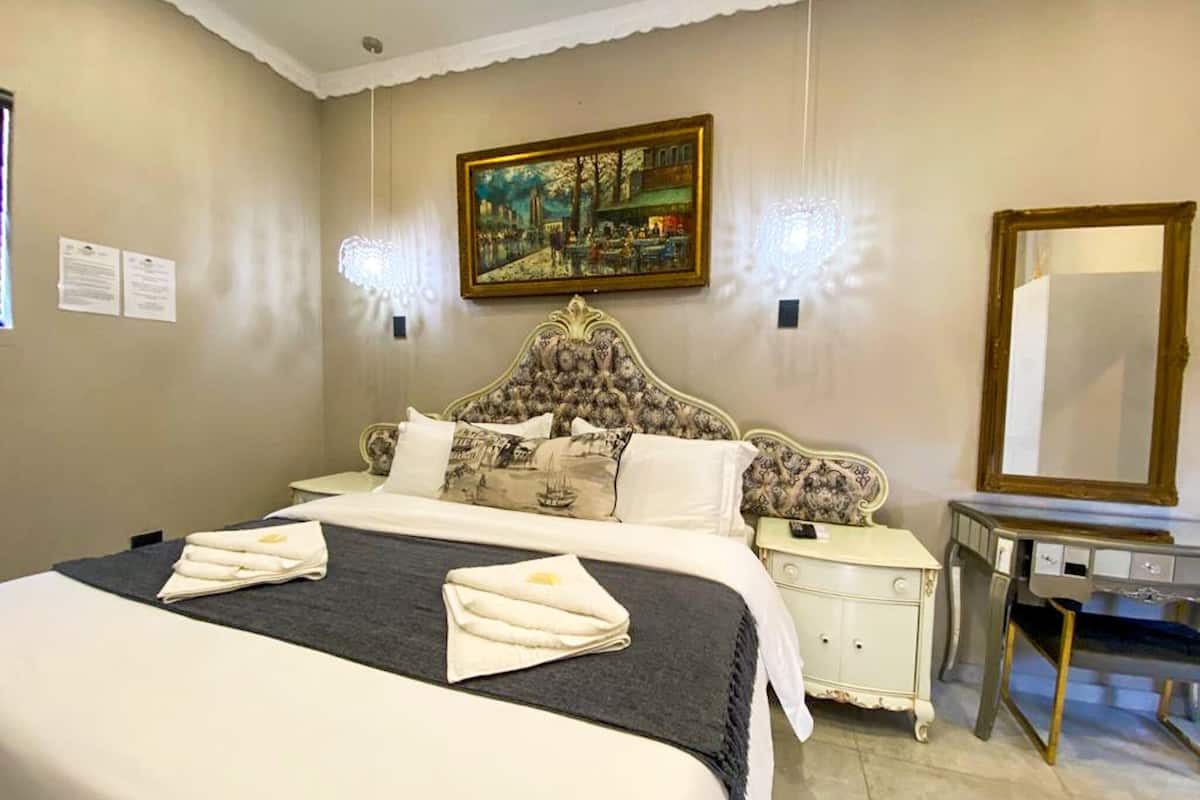 A hotel room with a large bed, a nightstand, a dresser, a painting on the wall, and a mirror.